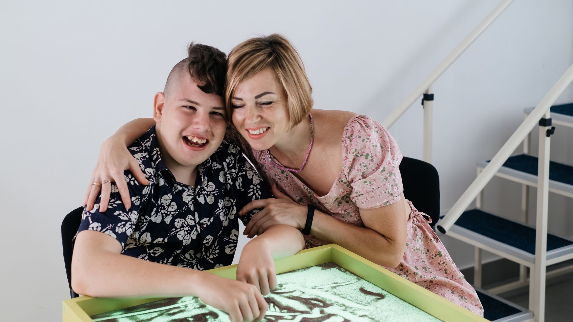 A therapist and young adult with disabilities enjoying an interactive light therapy session, showcasing effective engagement and joy in therapeutic activities.
